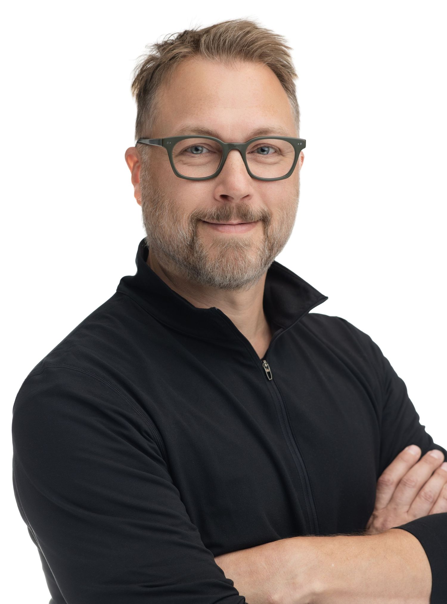 Professional man with glasses and beard, arms crossed, wearing black zip-up top, against white background.