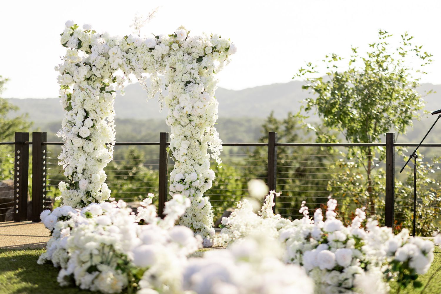 Romantic white flower wedding arch set up for outdoor mountain ceremony.