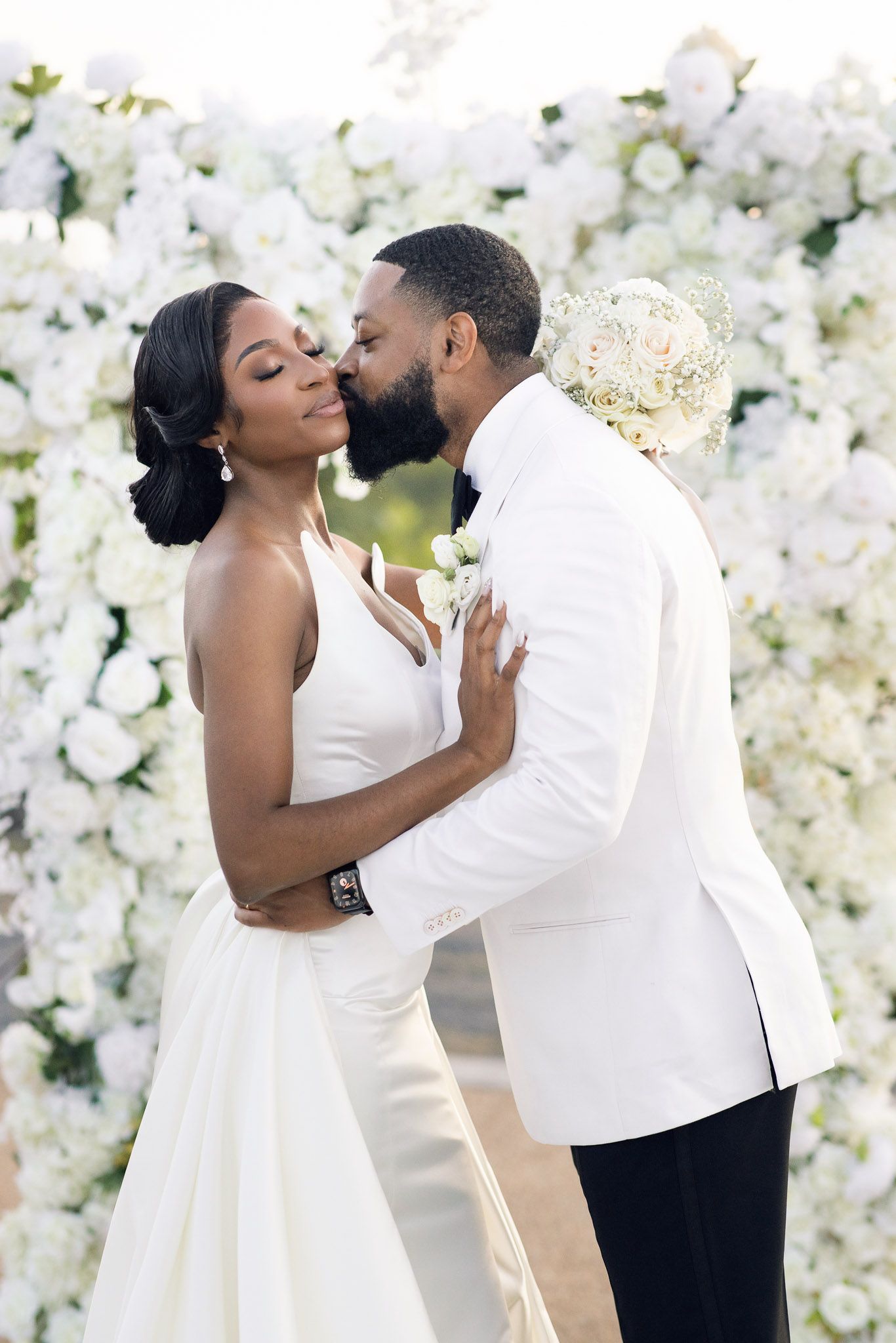 Romantic wedding couple shares intimate moment against backdrop of white flowers.