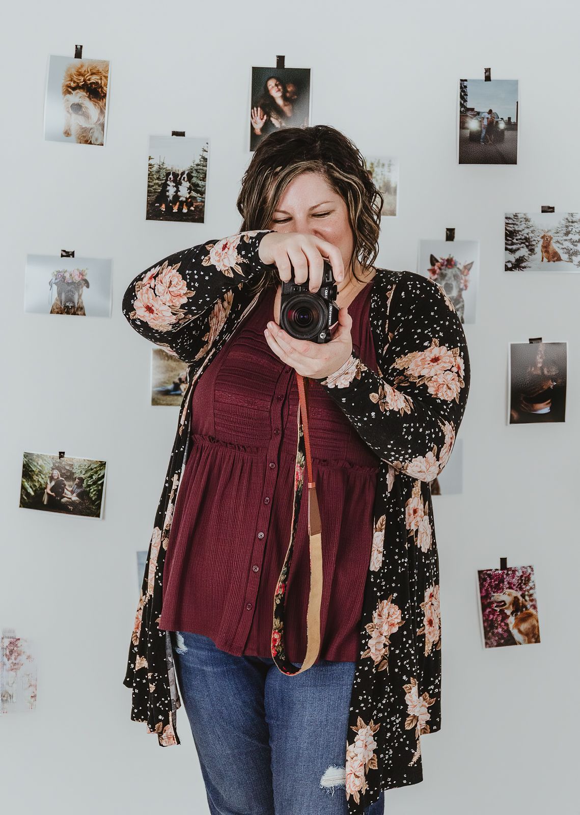 Edmonton area photographer Coral Konanz smiling with camera in studio surrounded by client artwork