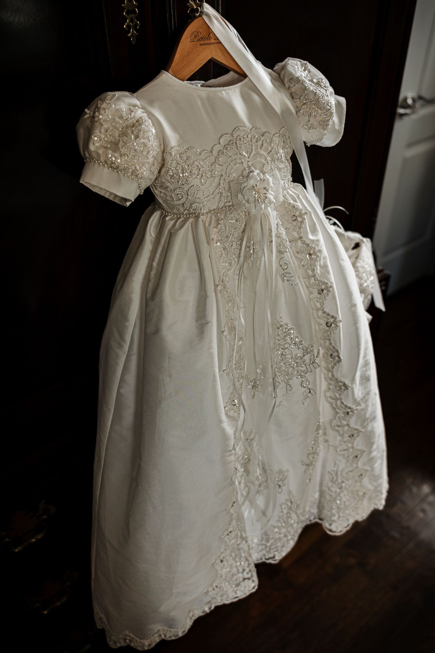 Elegant white baby christening gown with lace trim and puff sleeves hanging on a wooden hanger.