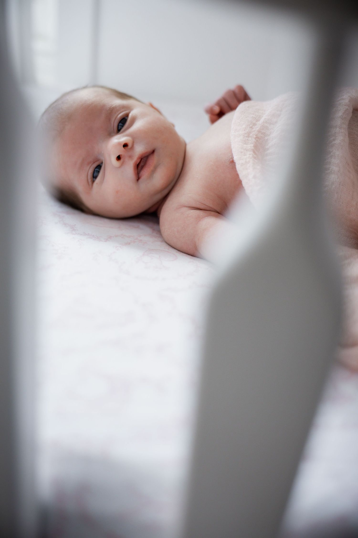 Newborn baby lying in white crib looking up with curious eyes in Staten Island.