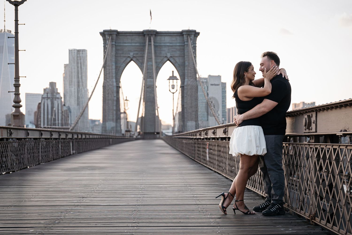 Couple sharing a romantic moment on the Brooklyn Bridge with NYC skyline in the background.