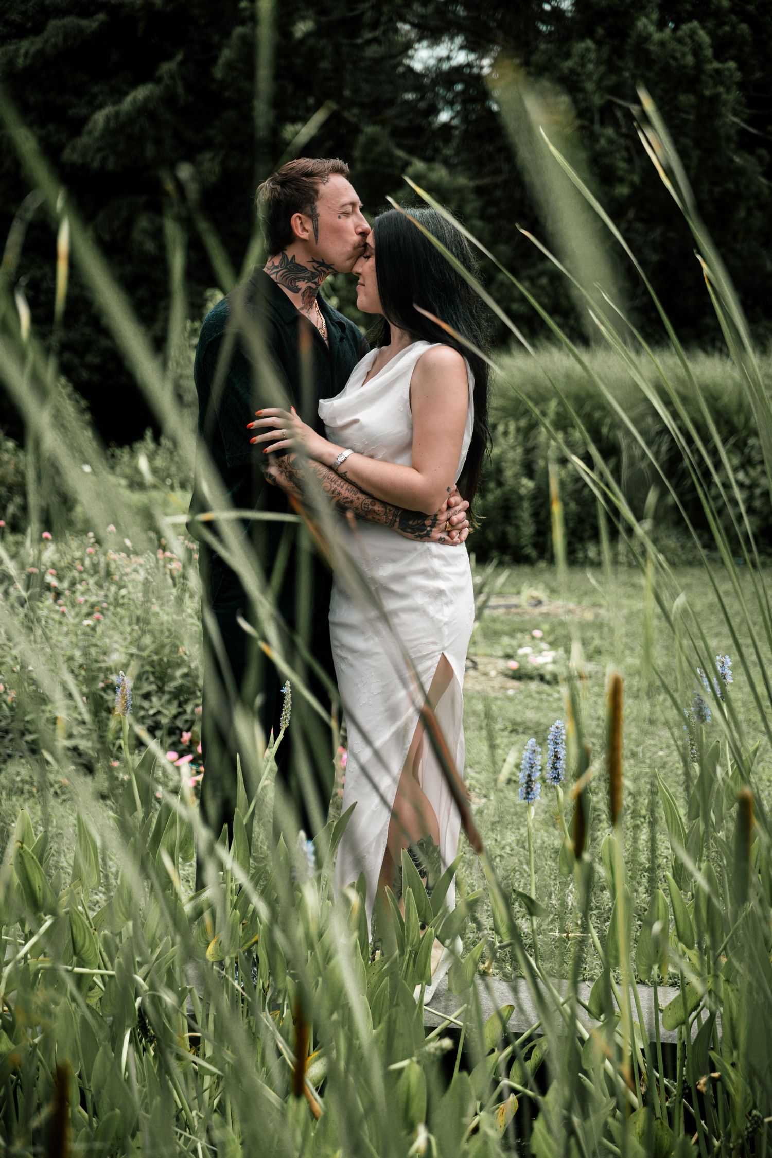 Couple sharing a tender kiss while embraced in a wildflower meadow with tall green grass.