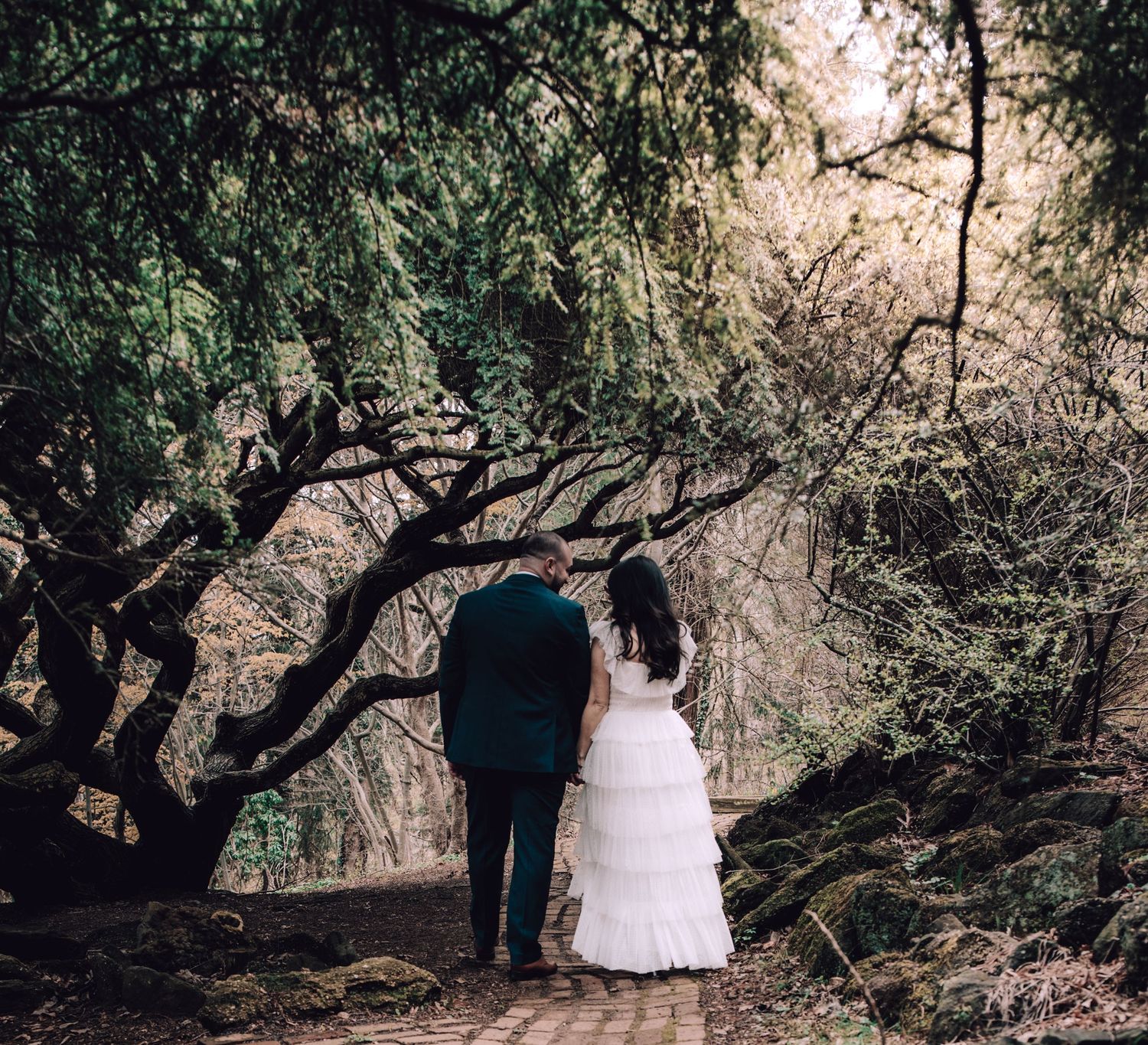 Newlywed couple walking hand in hand along wooded forest path in wedding attire in New Jersey.