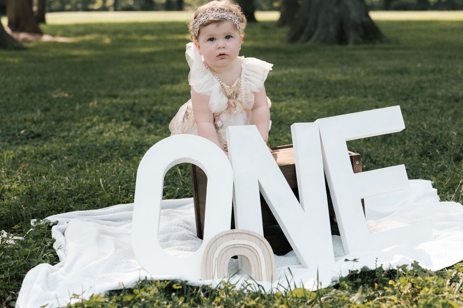 Baby girl in ruffled dress sitting with large white ONE letters for first birthday photo shoot.