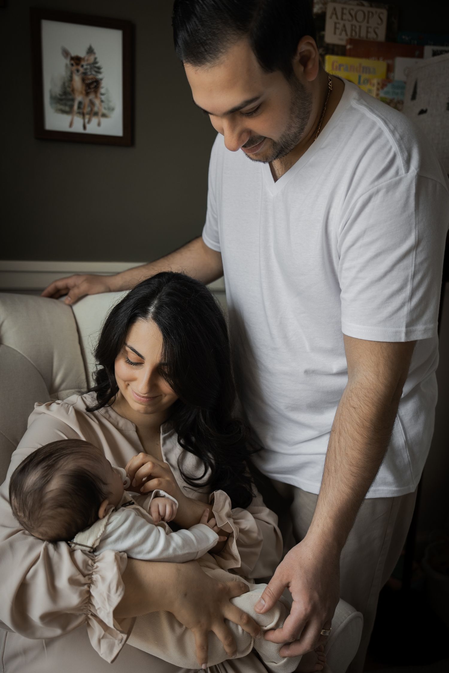 New parents admire their newborn baby together in a cozy, book-filled nursery room.
