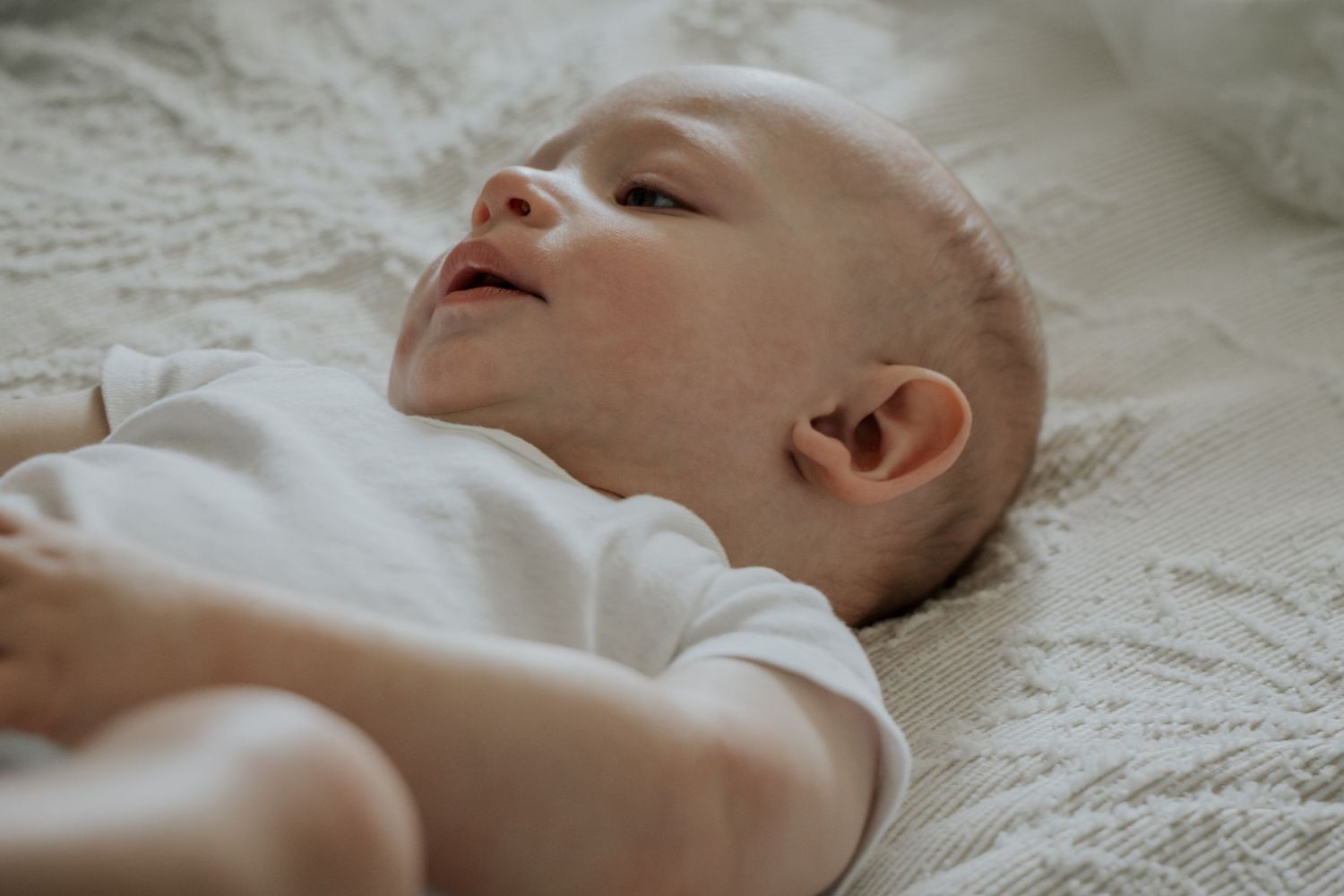 Peaceful newborn baby lying on white blanket looking up.