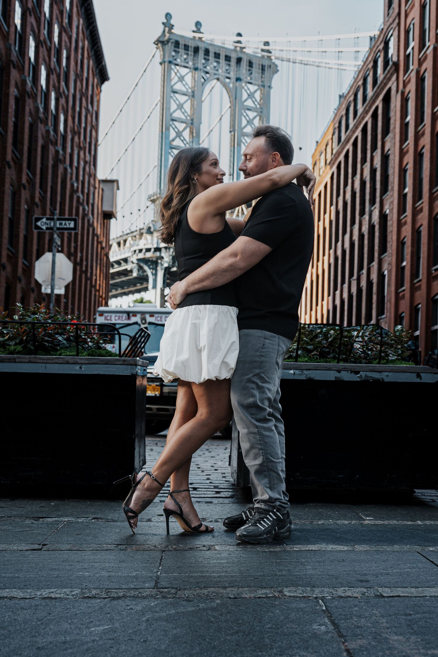 Couple embracing and dancing in DUMBO Brooklyn with Manhattan Bridge in background.