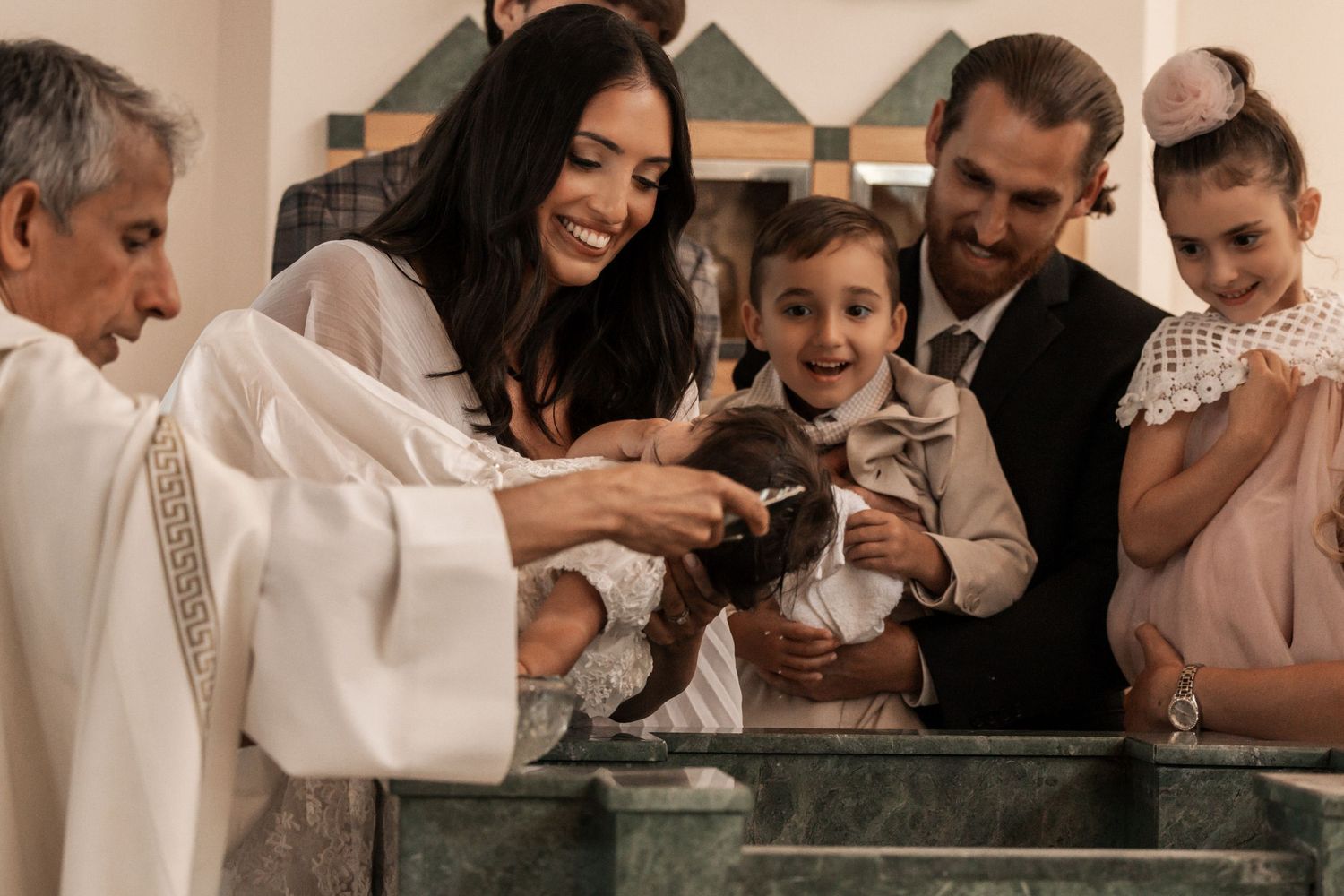 A joyful family gathers around the baptismal font as a priest performs a christening ceremony in church.
