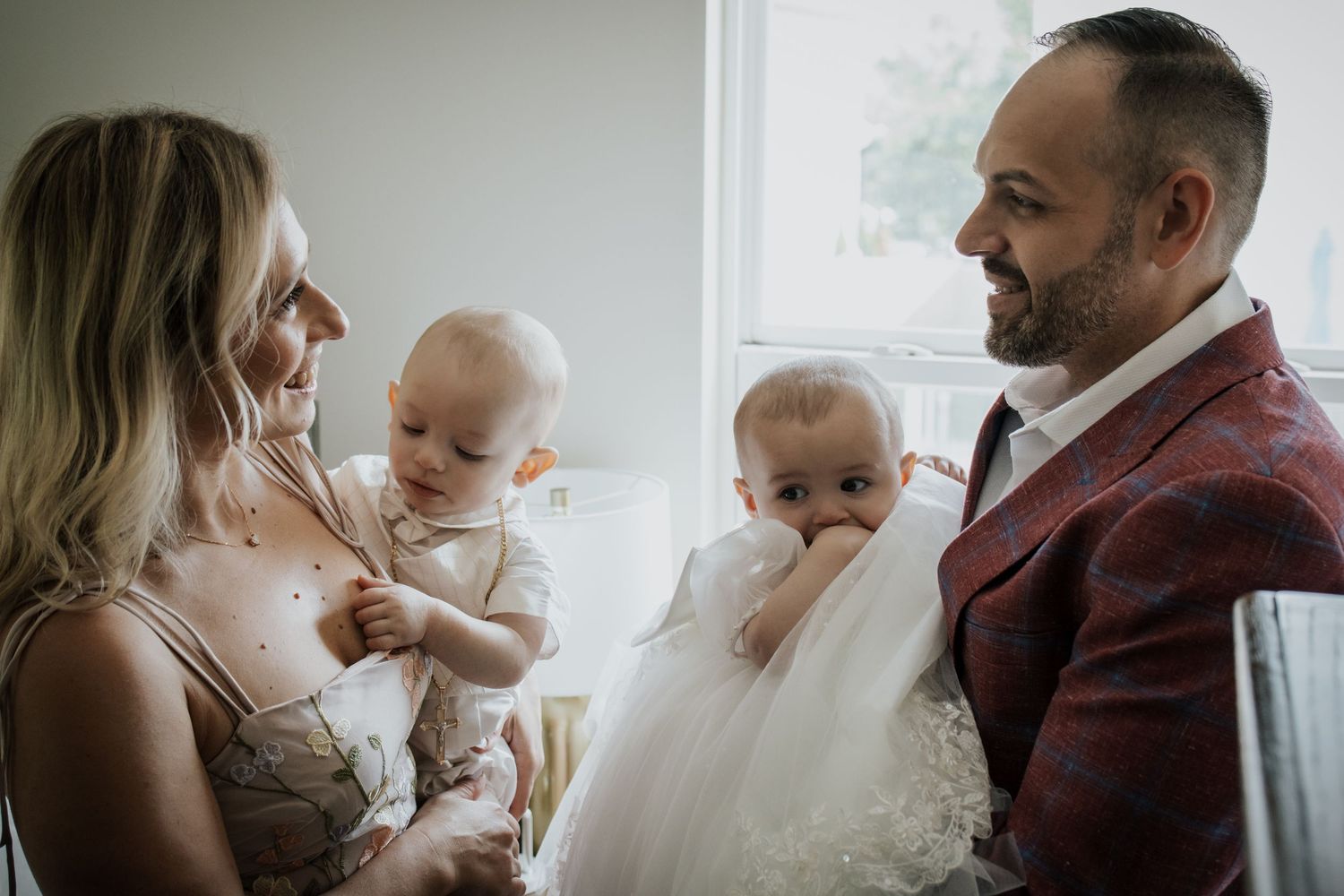 Parents sharing a tender moment with two babies in white outfits.