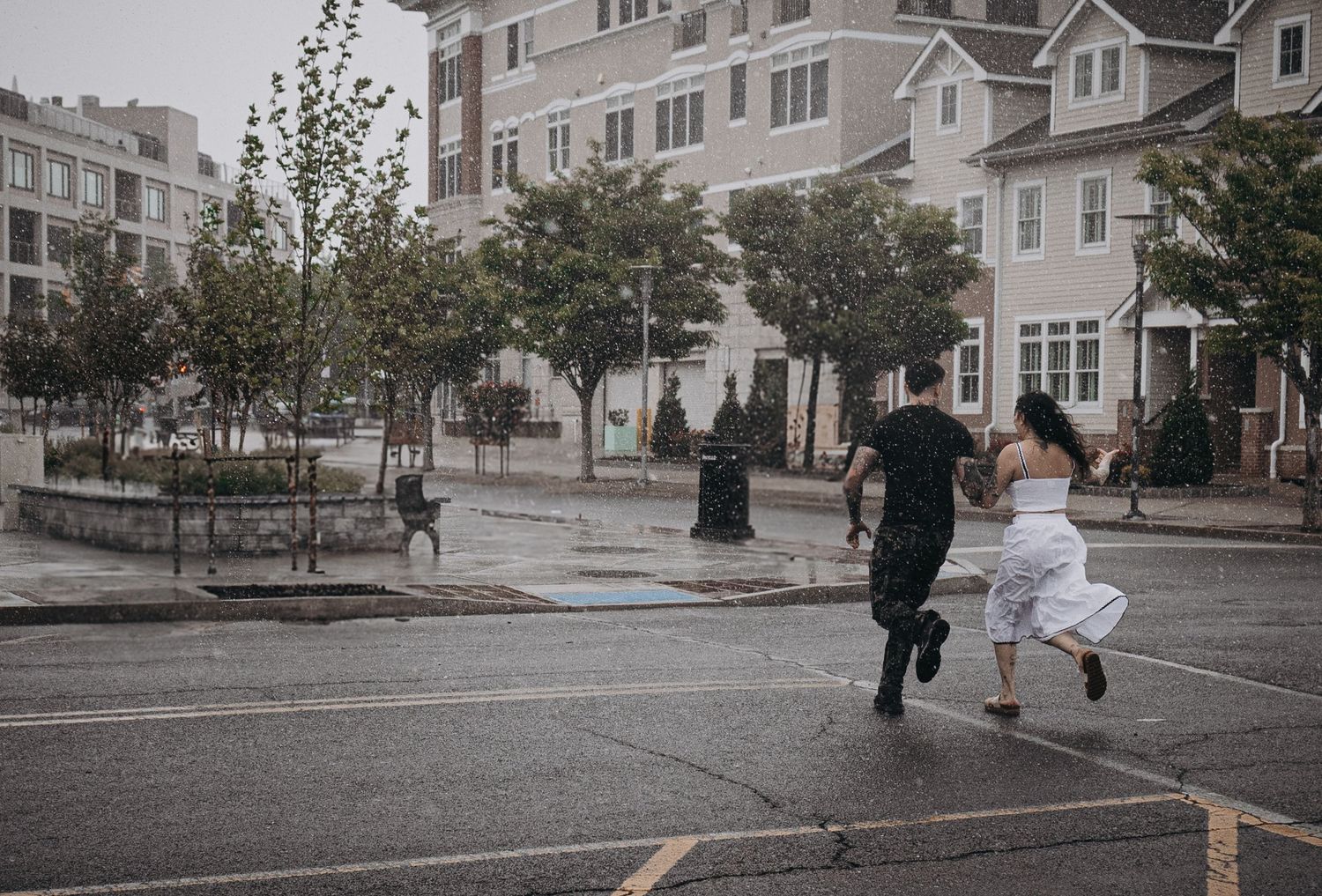 Couple running through rainy urban street in wedding attire during outdoor photo session in New Jersey.