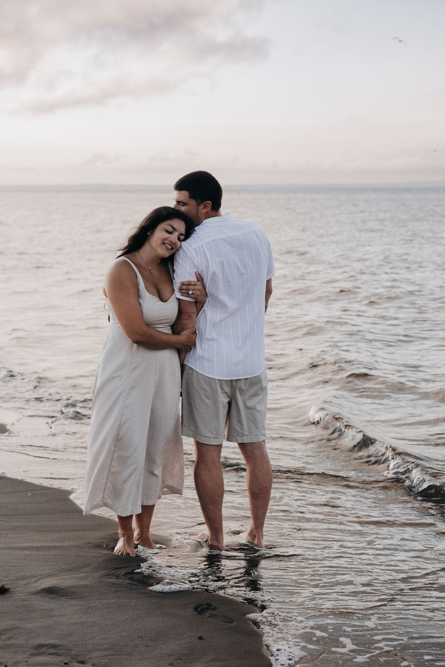 Romantic couple embracing at ocean's edge during peaceful sunset on beach.