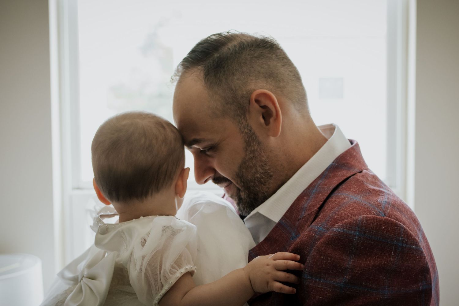 Father tenderly holding baby in white christening outfit.