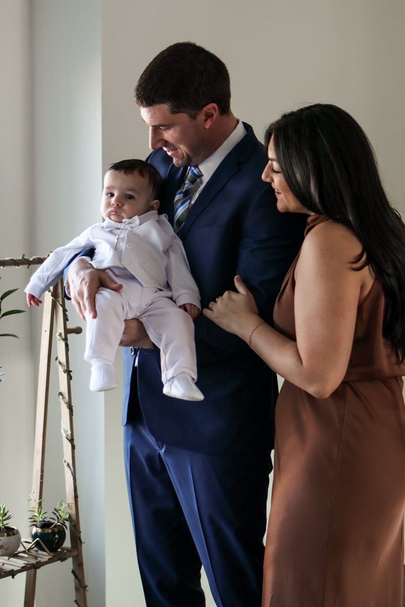 Couple in elegant formal wear smiling at their baby boy during a christening photo session.