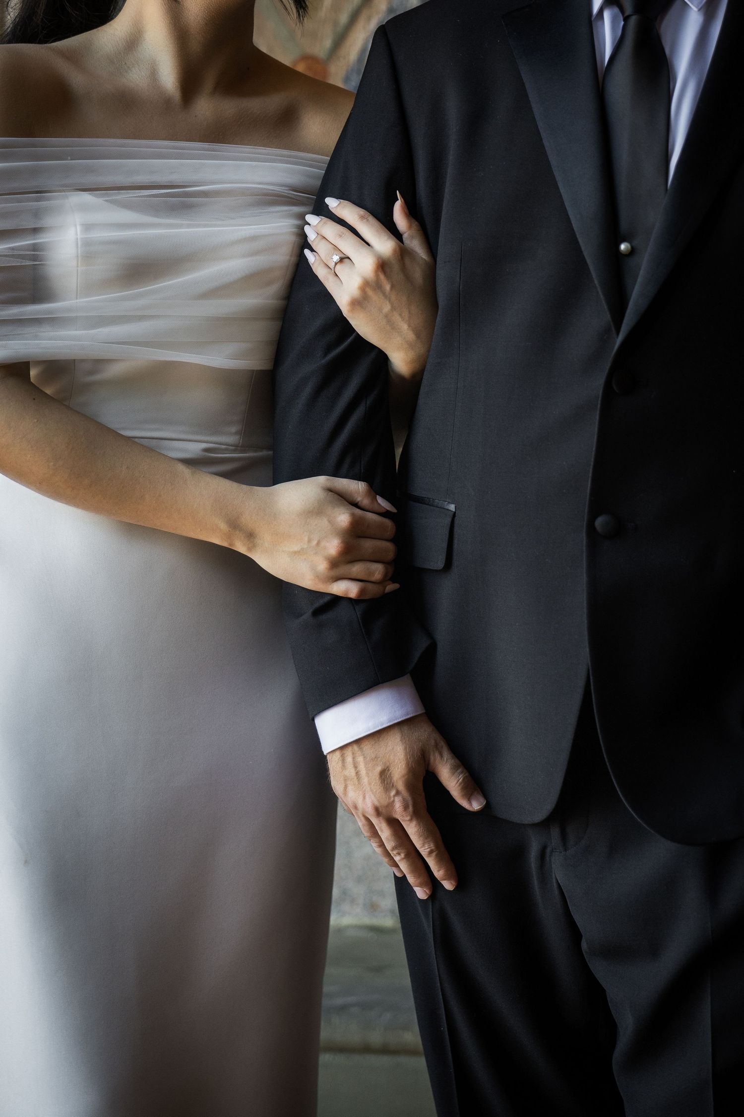Close-up of bride in flowing white gown holding grooms arm showing diamond engagement ring detail in New Jersey.