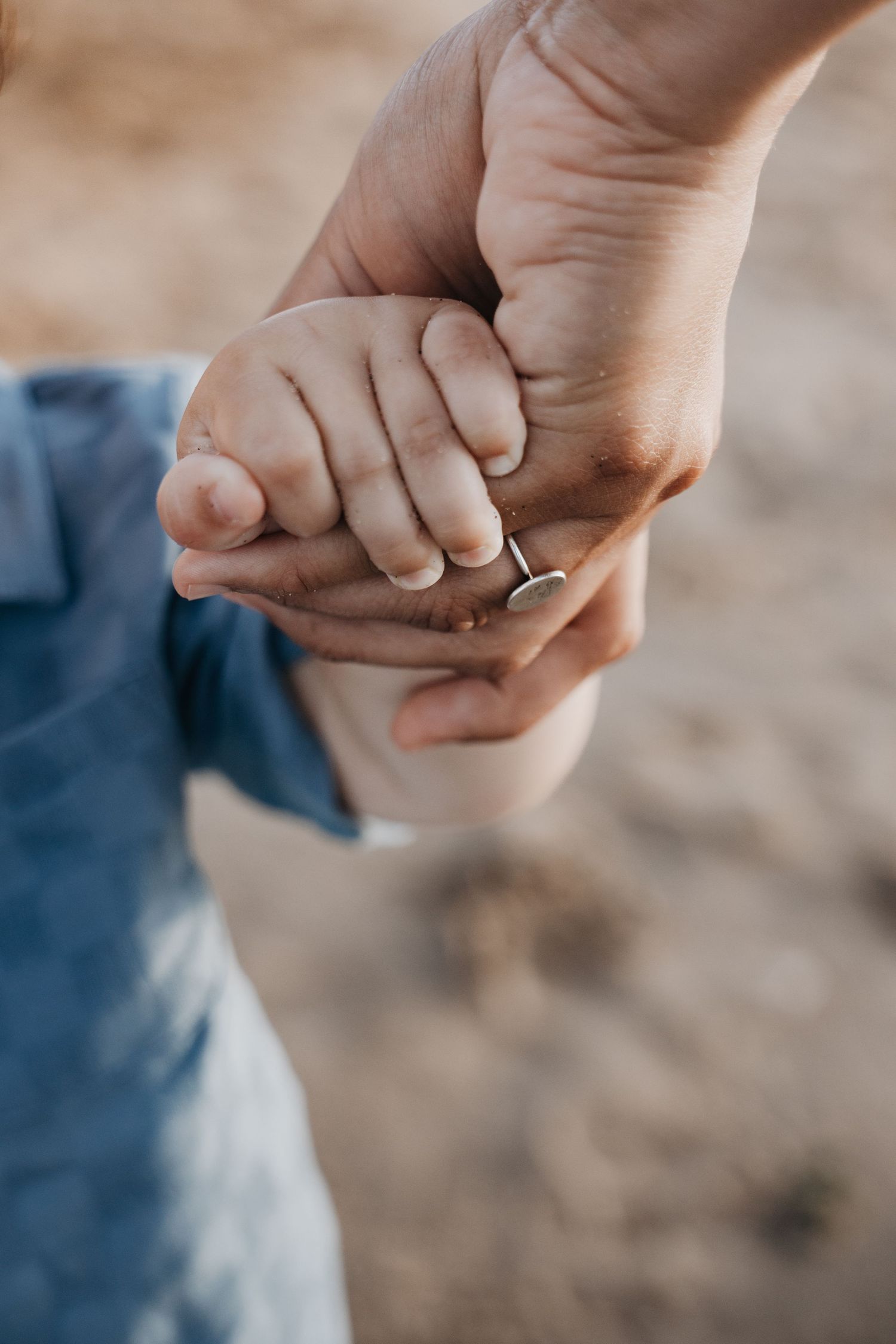 Close-up of adult hands gently holding small baby hand outdoors.