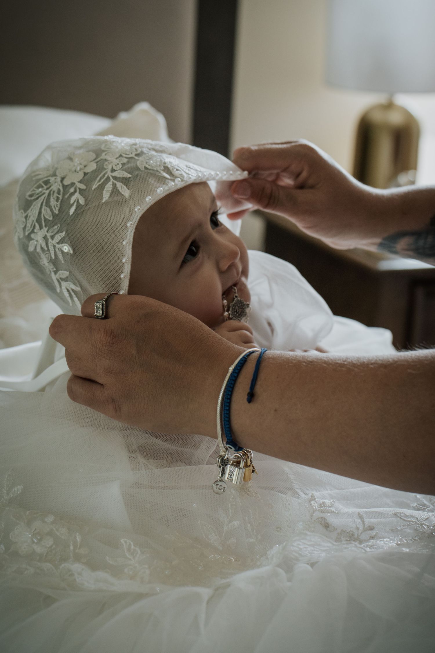 Adult hands placing lace christening bonnet on baby.