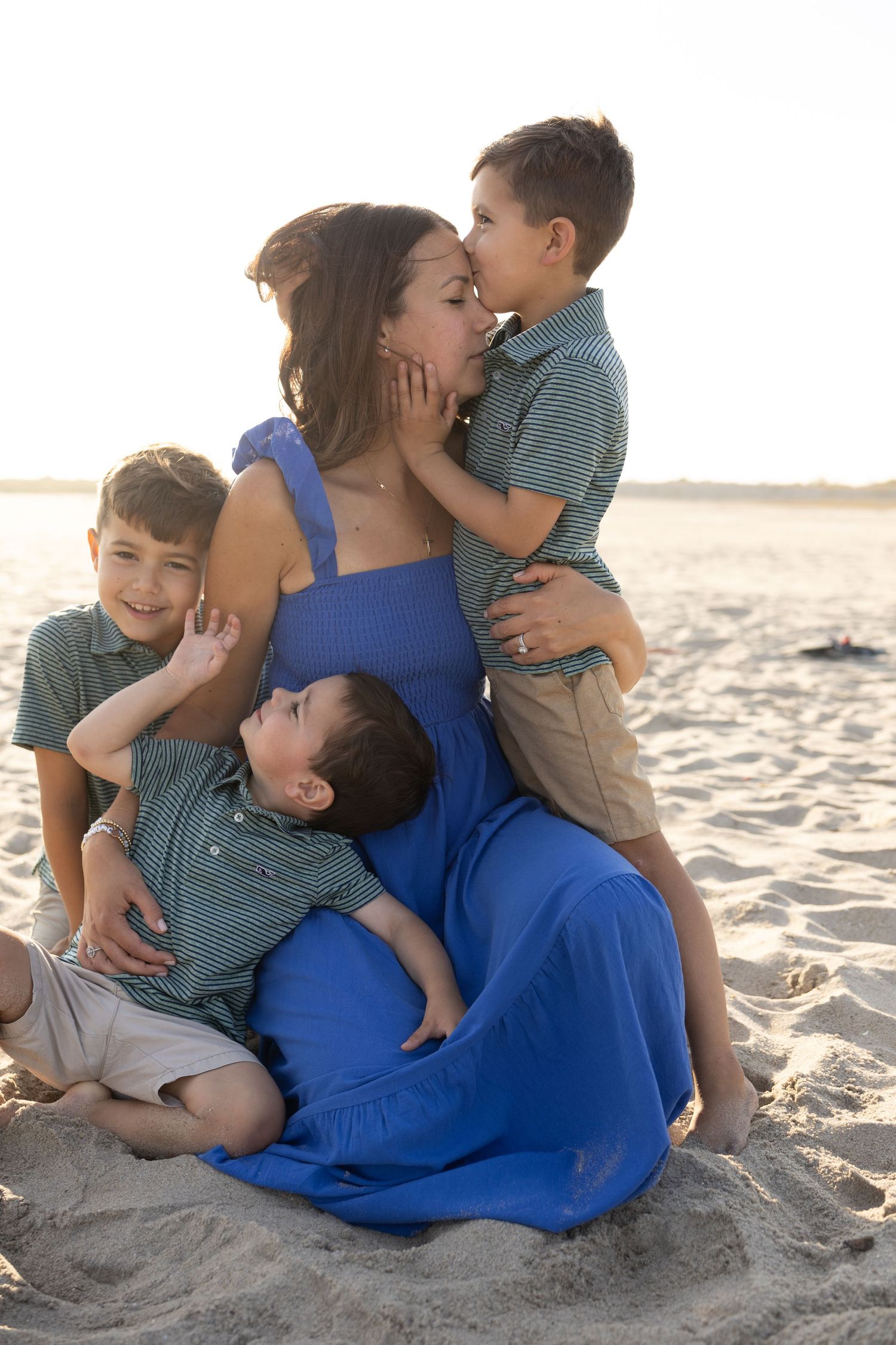 Mother in blue dress with three children on sandy beach at sunset.