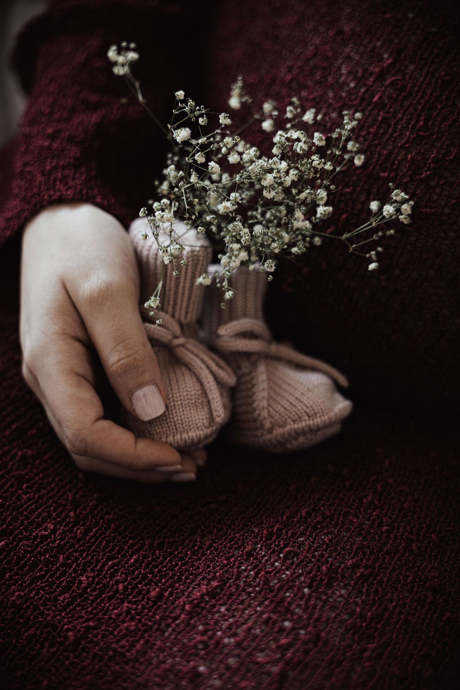 Close-up of pregnant woman holding tiny knit baby booties with delicate white flowers inside.