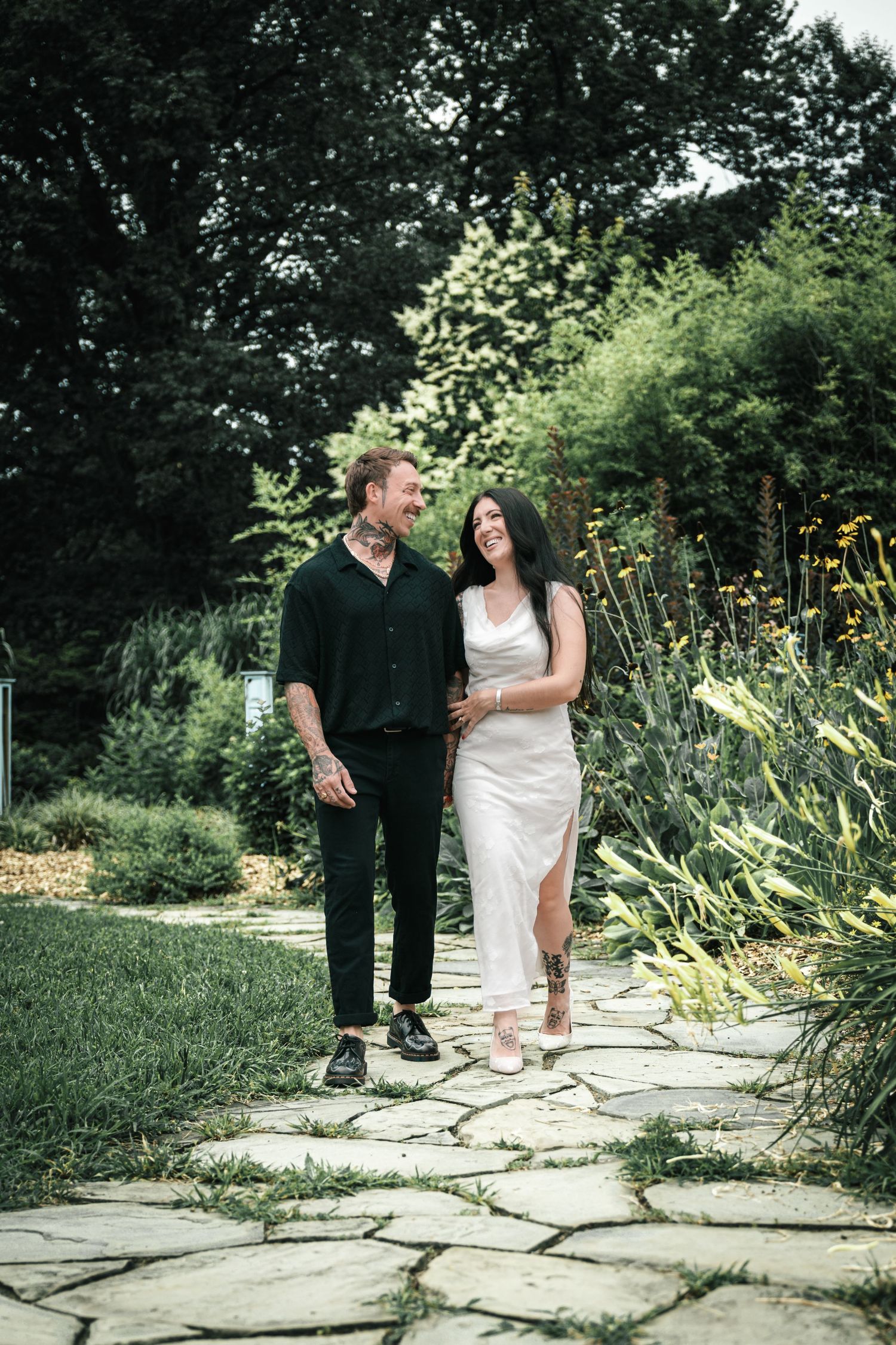 Happy couple walking together on a stone path through a lush garden, laughing and smiling.