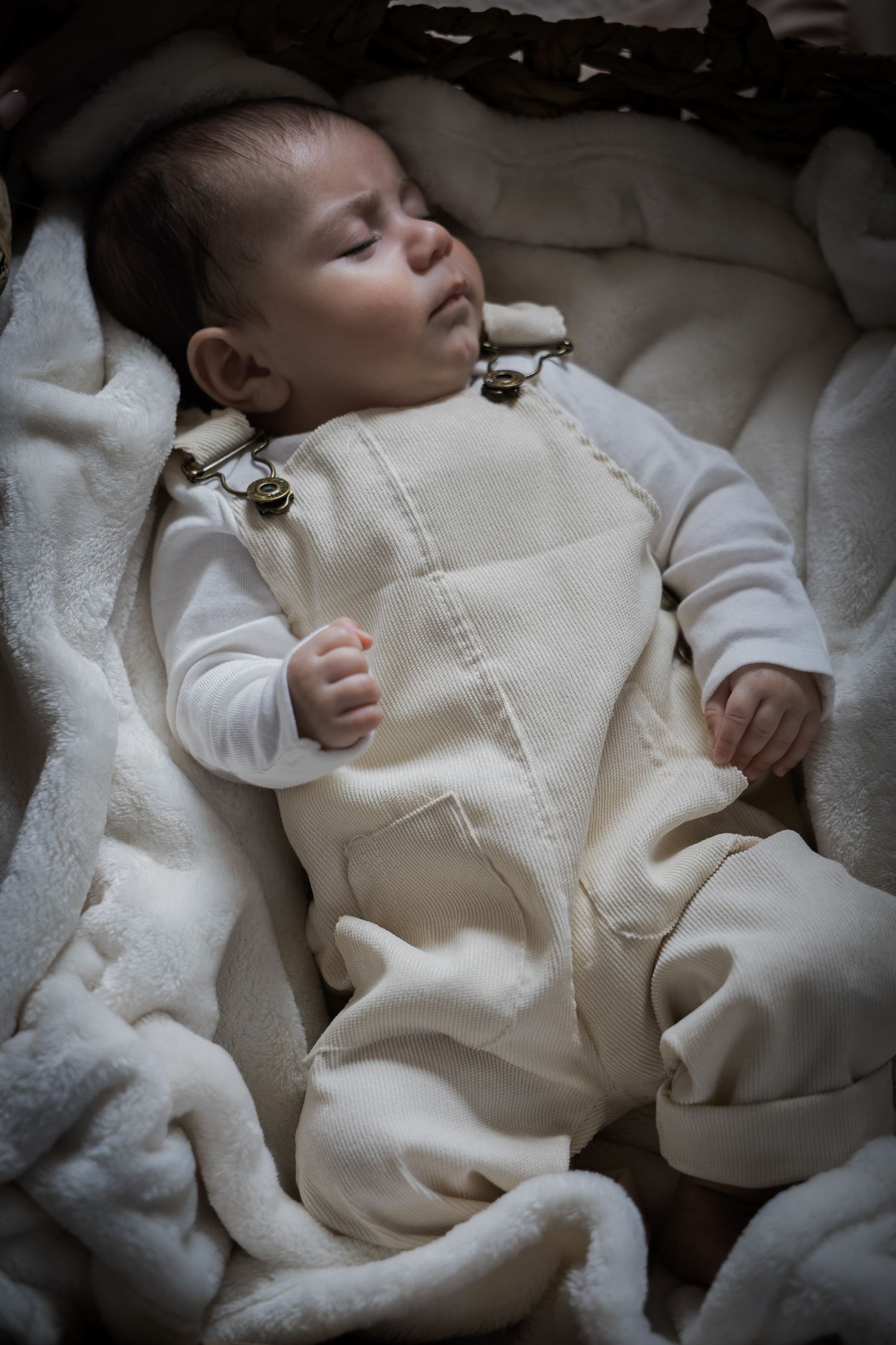 Peaceful newborn baby sleeping in a cream outfit inside a cozy basket.