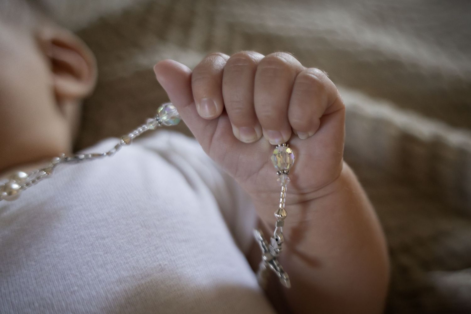 Newborn baby hand gently holding a pearl rosary during baptism or christening ceremony.