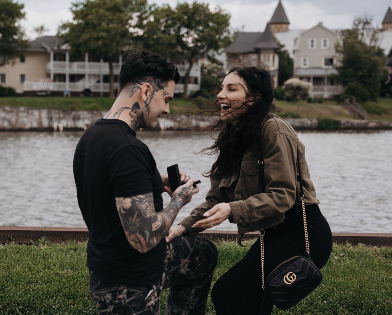 Tattooed man proposing to surprised woman near waterfront during outdoor engagement moment in New Jersey.
