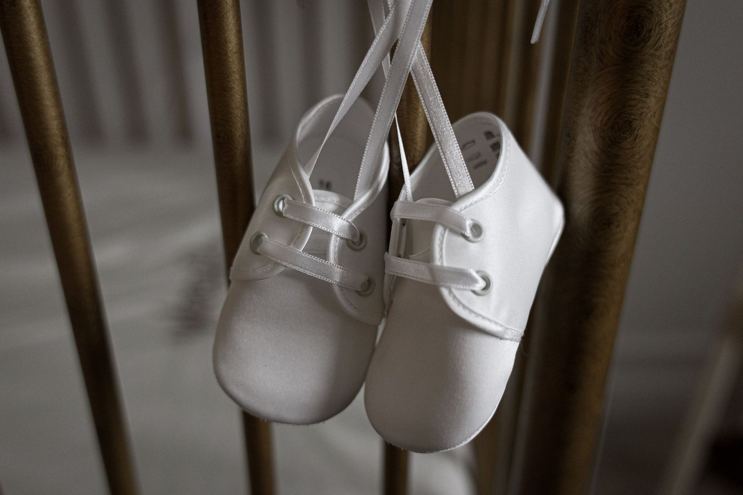 White baby shoes hanging on gold crib rails for a christening ceremony.