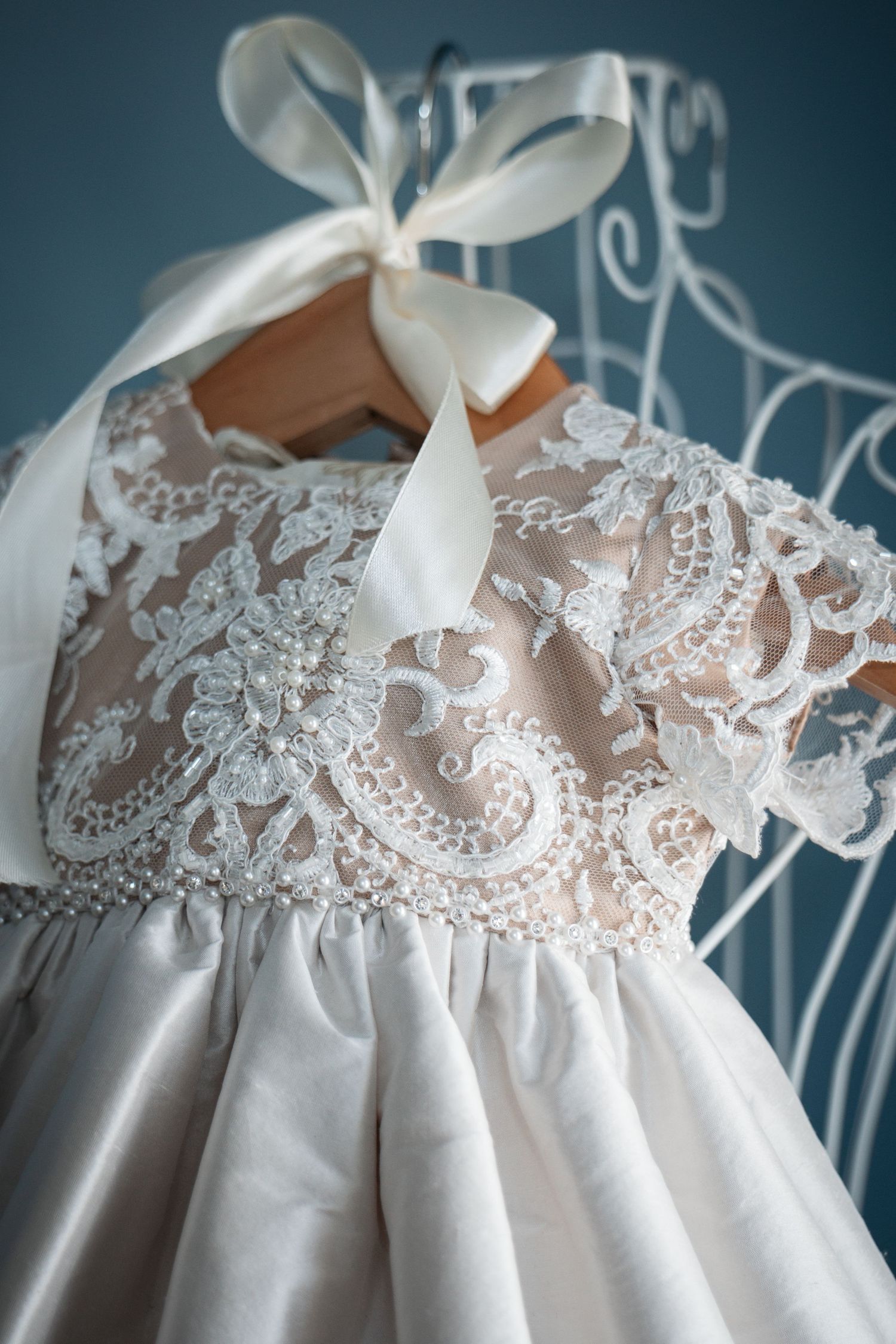 Close-up of intricate pearl and lace embroidered bodice on white silk christening gown.