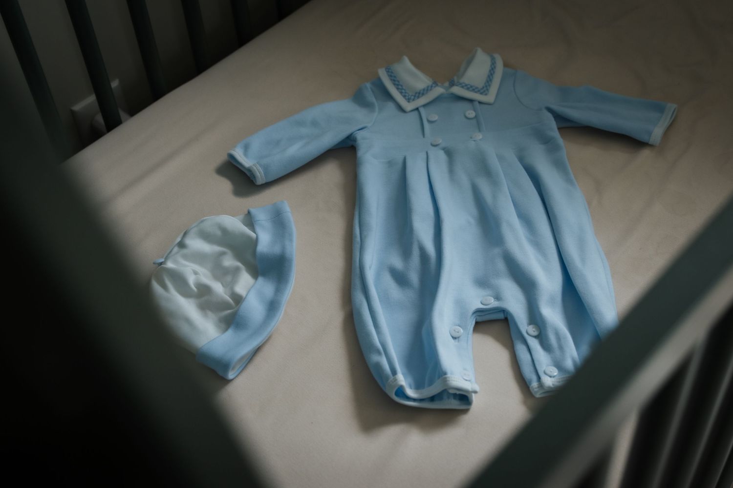 Light blue baby romper and matching striped hat laid flat in white crib.