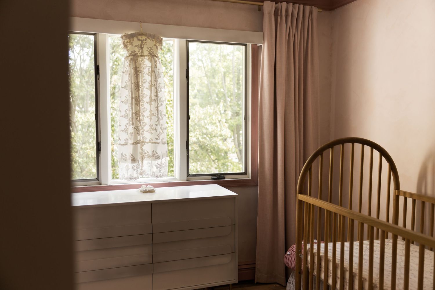 A serene nursery with a wooden crib, white dresser, and natural light streaming through sheer curtains.