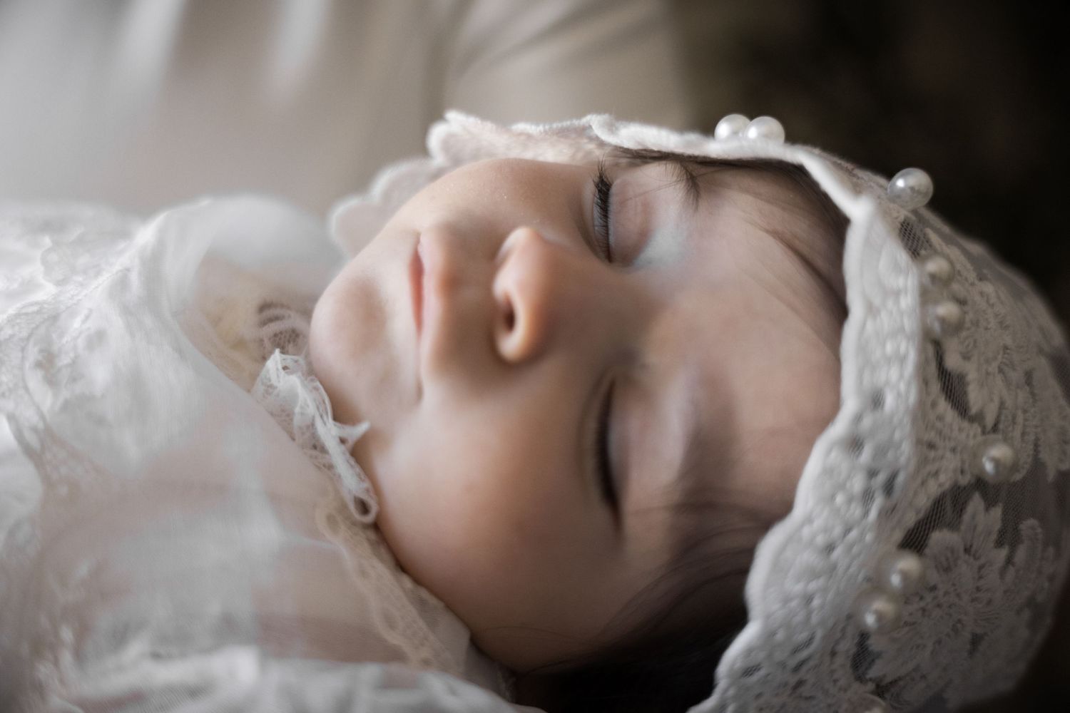 Peaceful sleeping newborn baby wearing a delicate white lace bonnet and christening outfit.