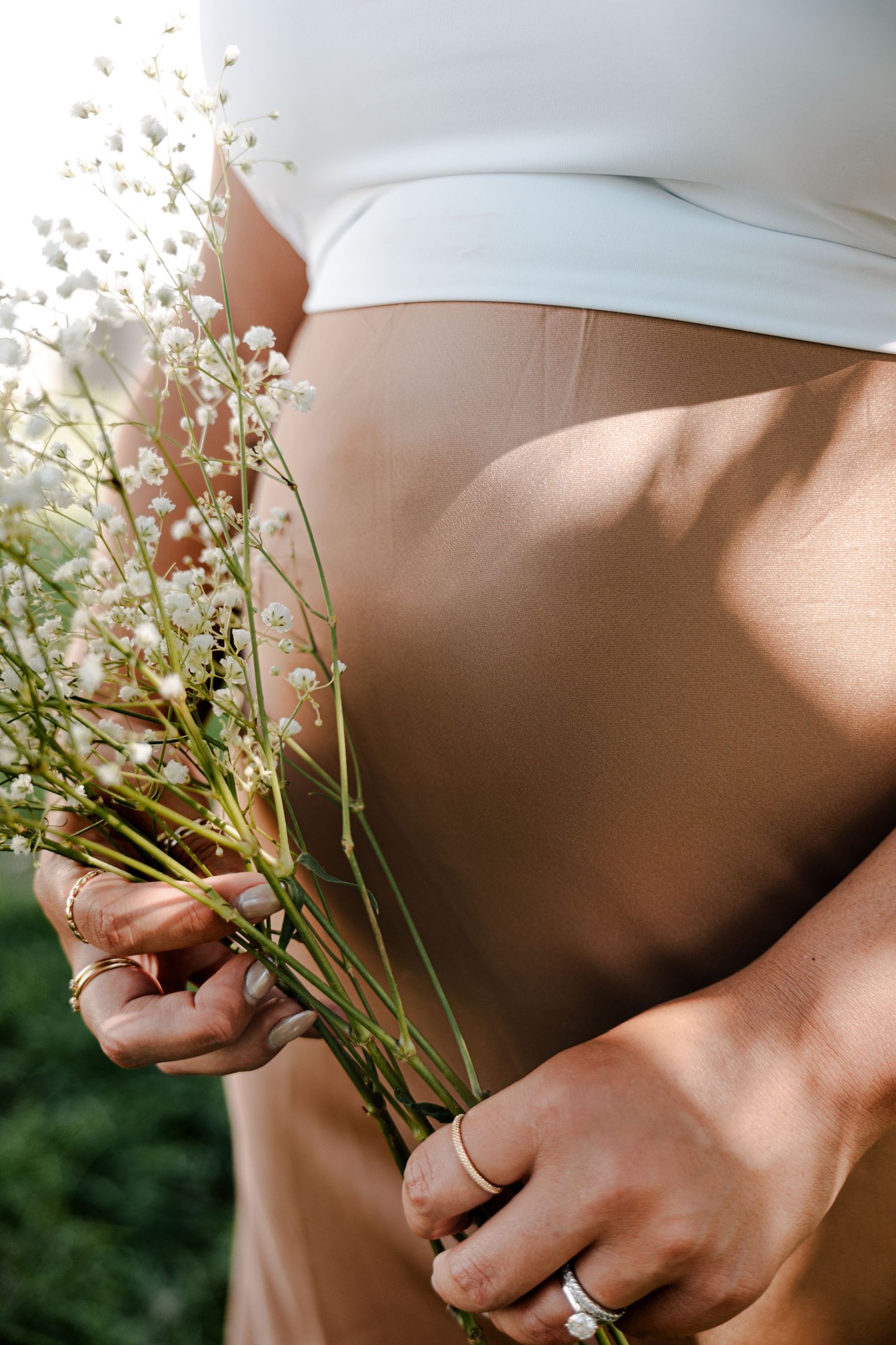 Close-up of pregnant belly with white wildflowers, maternity photo.