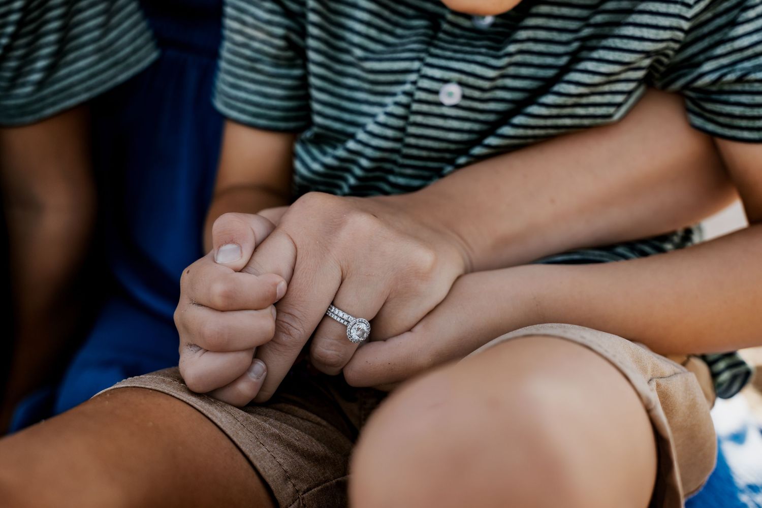 Close-up of couple holding hands with diamond engagement ring on beach.