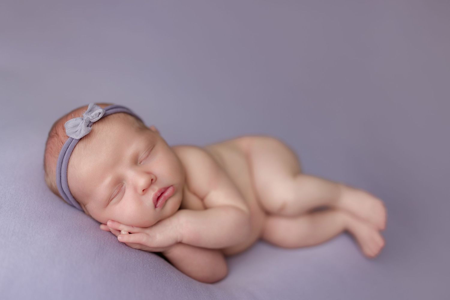 Artistic newborn photography with baby sleeping on purple background.