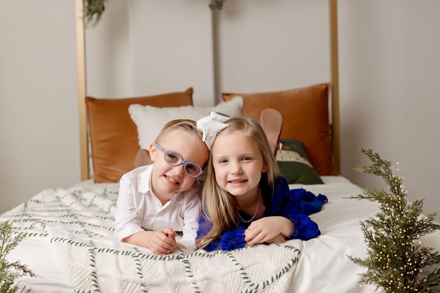 Two young children lying together on a white bedspread with holiday decorations.