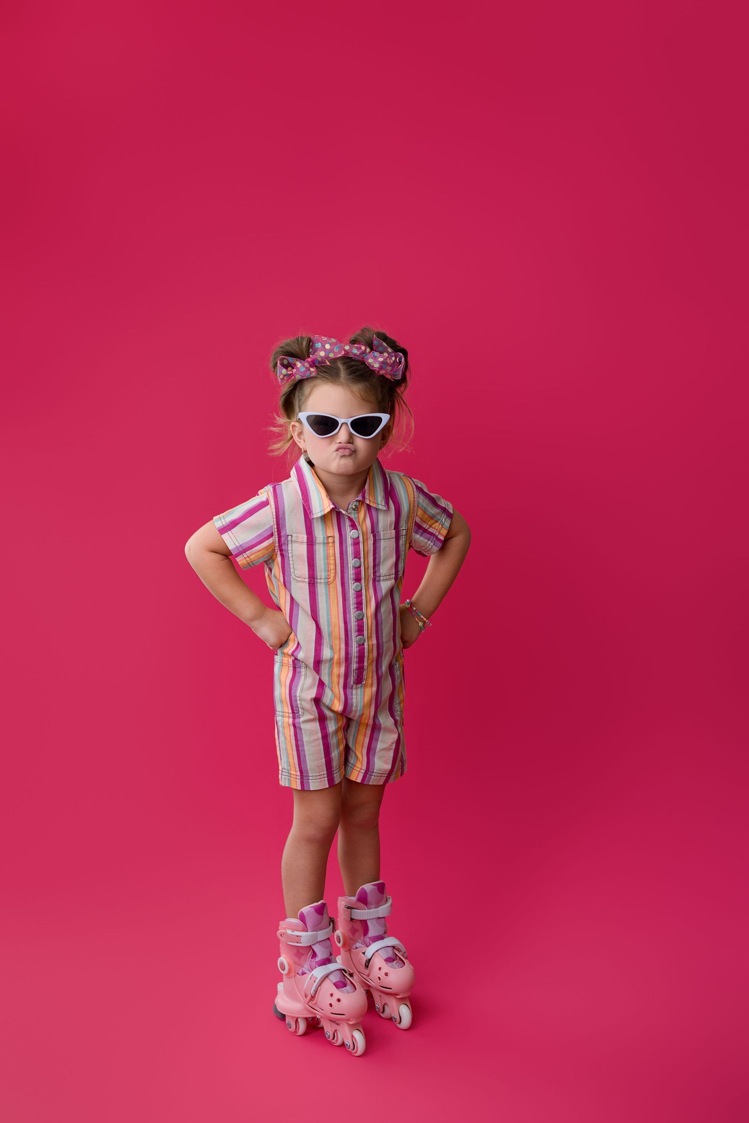 Small child wearing striped pink pajamas and matching cat ear headband poses confidently against bright pink backdrop.