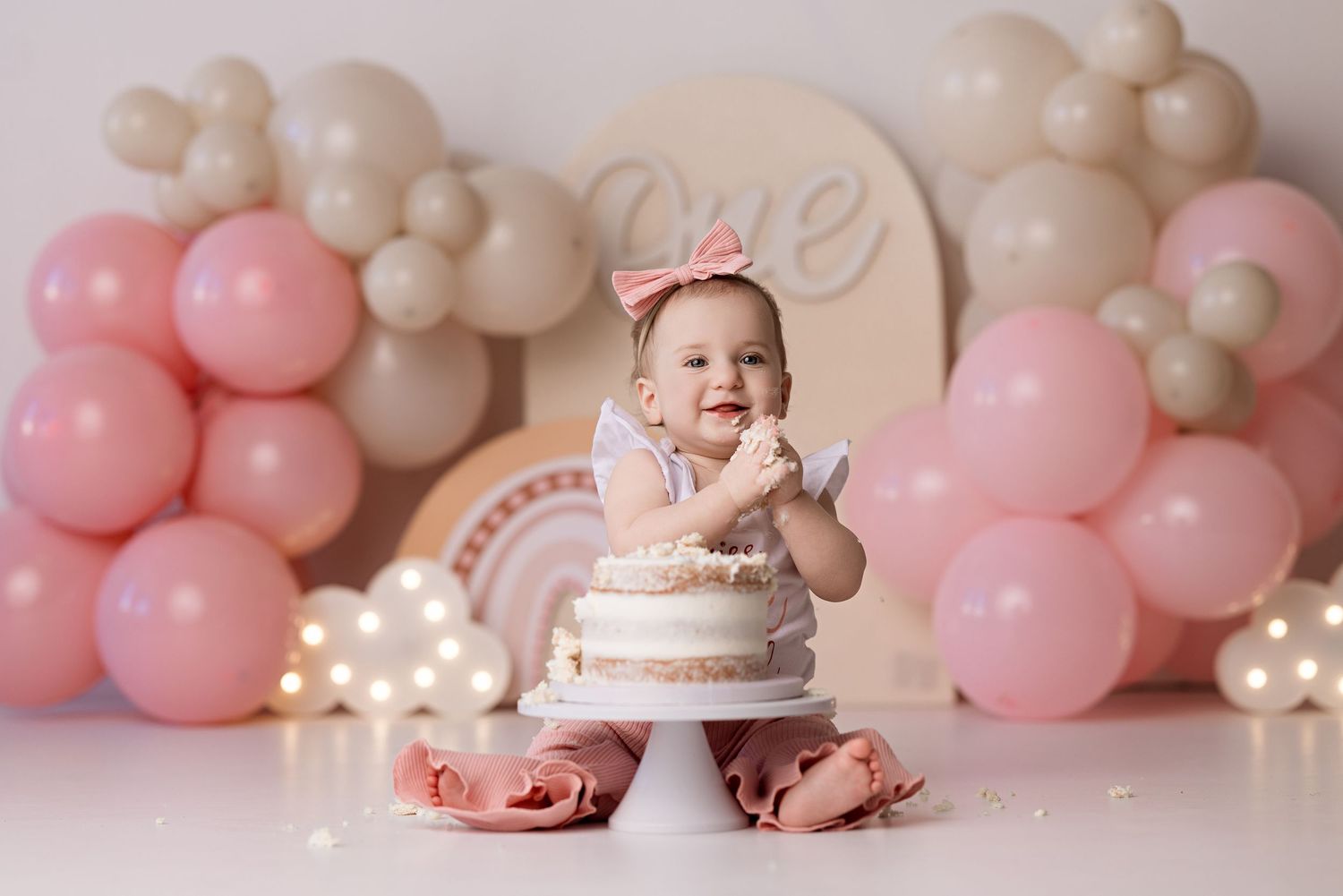 Pink and beige balloon arch backdrop with birthday cake and decorative elements for a first birthday celebration.