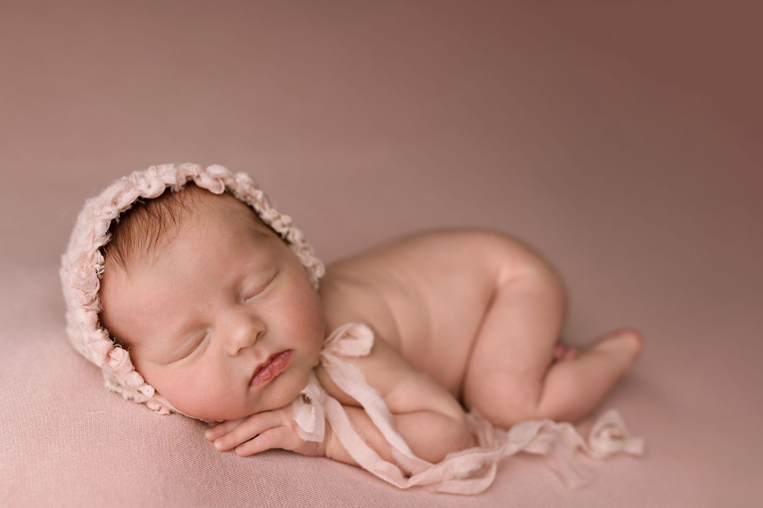 Soft pink studio backdrop with delicate floral and lace accessories for newborn photography.