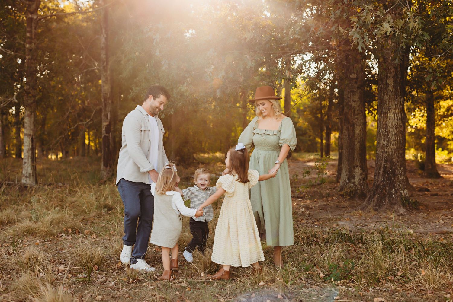 A family holds hands in a sunlit forest clearing during golden hour.