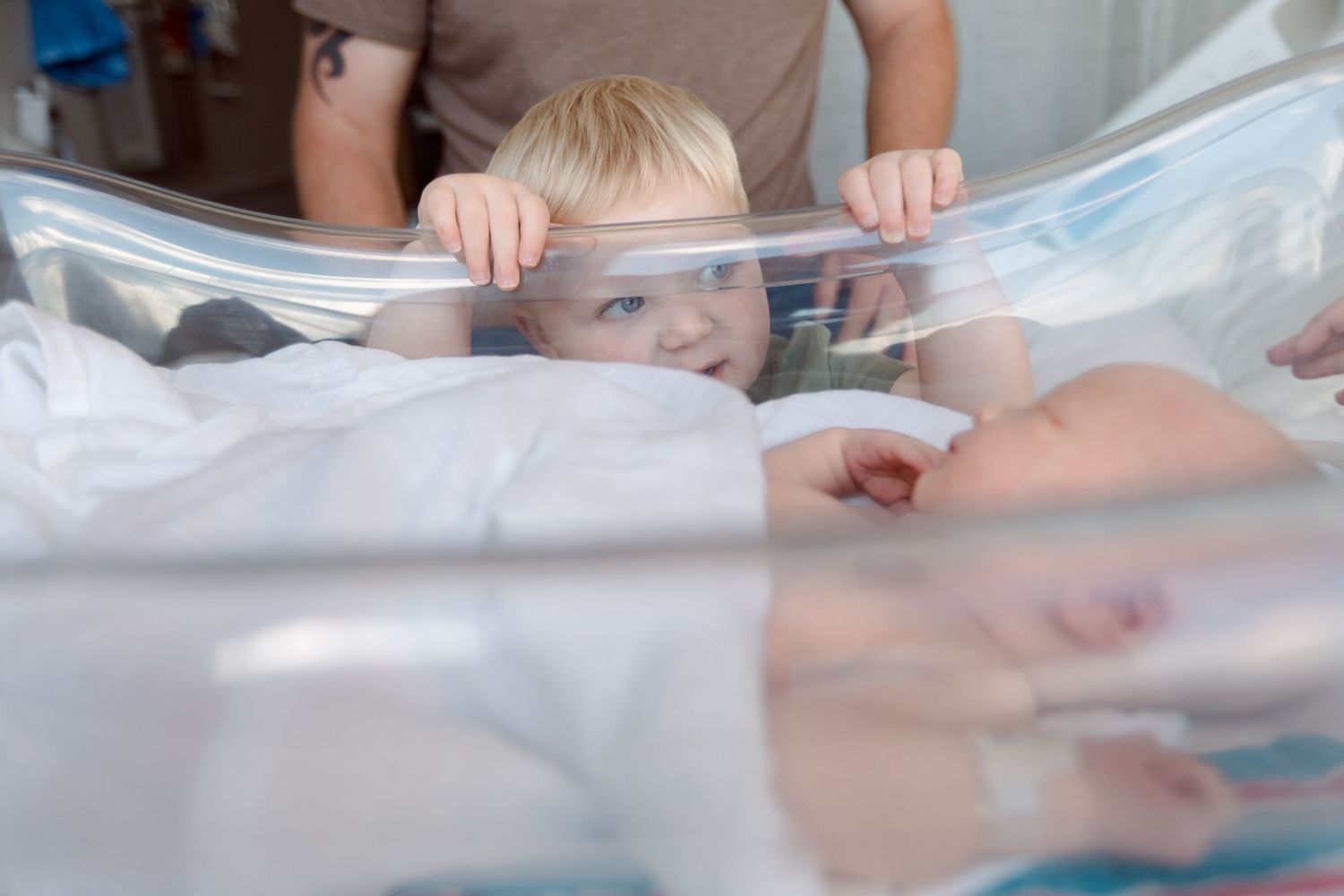 A person's hands gently wrap a newborn baby in soft white hospital blankets during Fresh 48 session in Beaumont hospital.