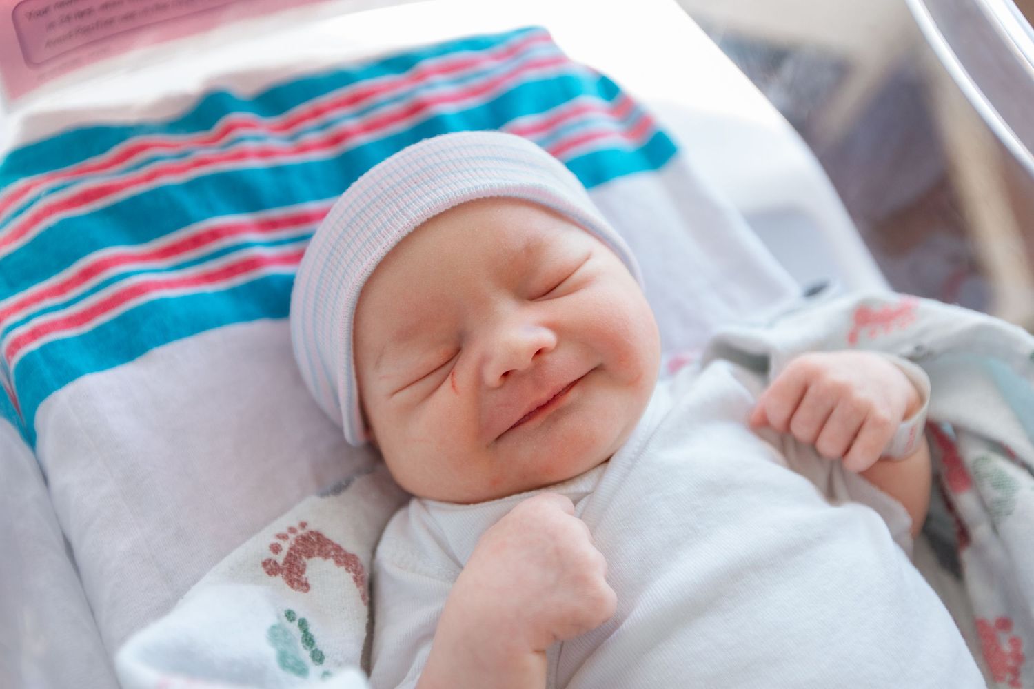 Sleeping newborn baby wearing striped hat and white onesie lies peacefully in bed during Fresh 48 session in Beaumont hospital.