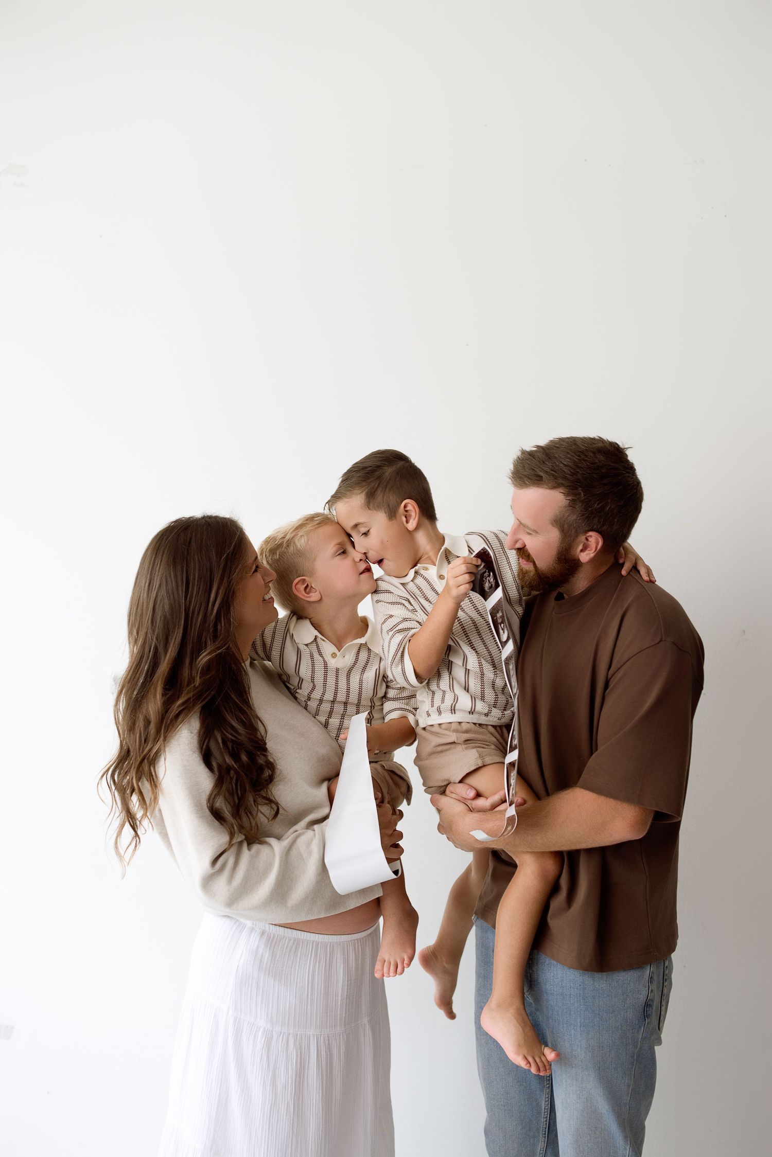 A family sharing a joyful moment together against a white wall in coordinating neutral-toned outfits.