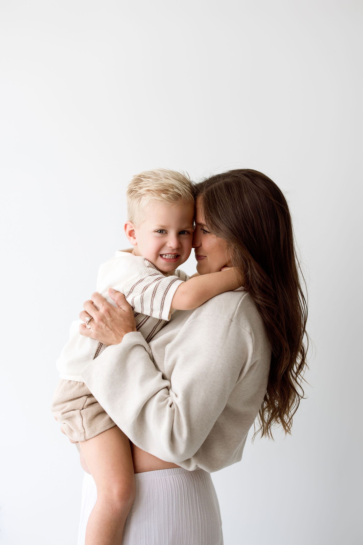 Tender moments captured in sequence showing a parent embracing a young child in matching beige outfits against white backdrop.