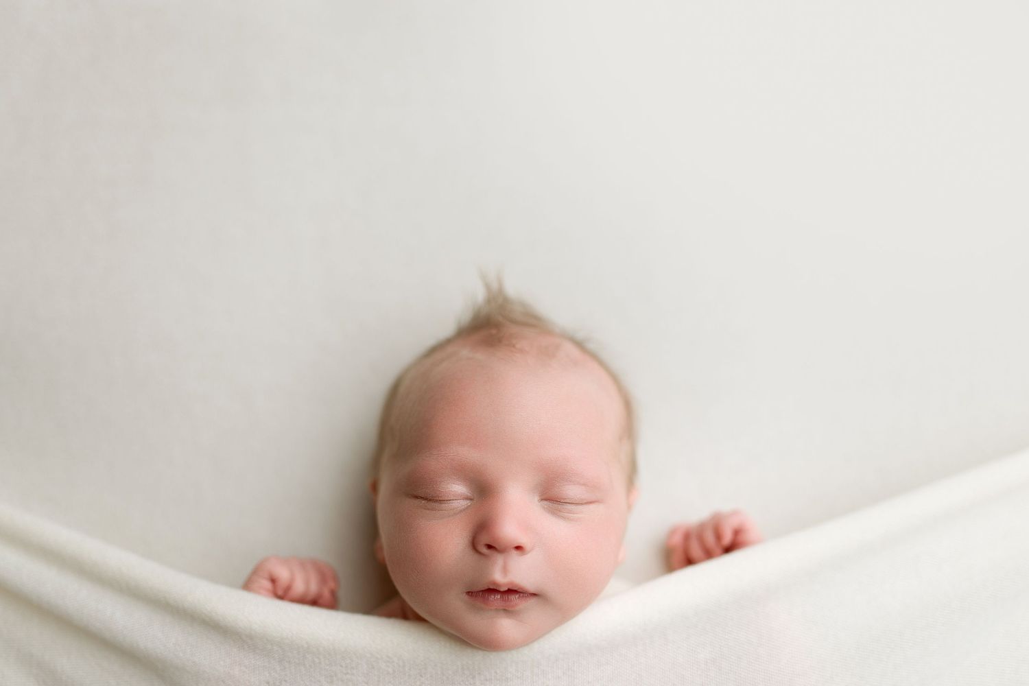 Sleeping newborn baby wrapped in white blanket photographed from different angles on light background.