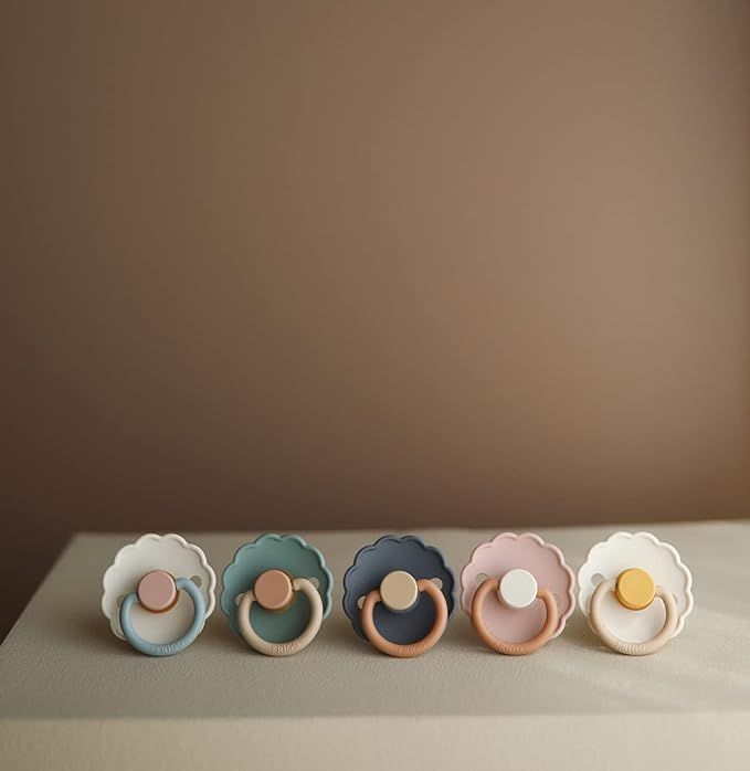 A row of pastel-colored clay rings with curved designs displayed against a neutral brown background.