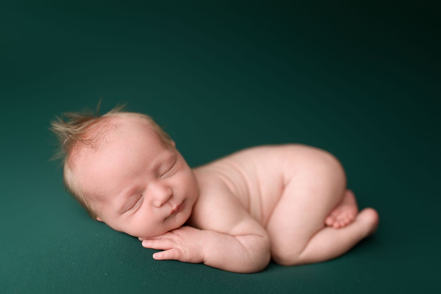 A series of seven artistic newborn baby photos against a dark green background showing different sleeping poses.