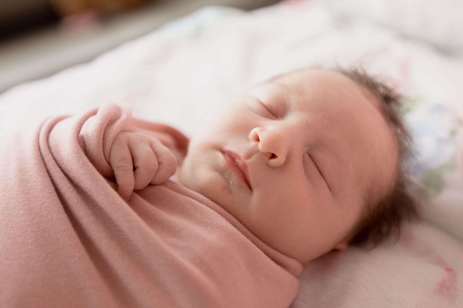 A peaceful newborn baby sleeping on soft pink bedding in natural window light.