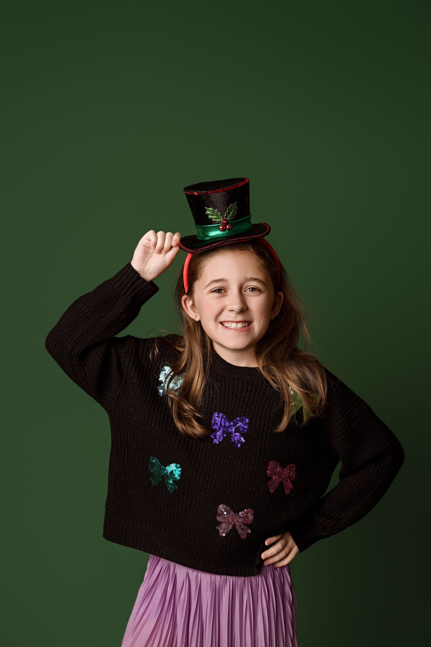 Child wearing black sweater with butterfly embellishments and pink skirt poses against dark green background.